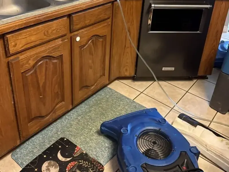 Air mover drying a kitchen floor in front of the cabinets after a leak