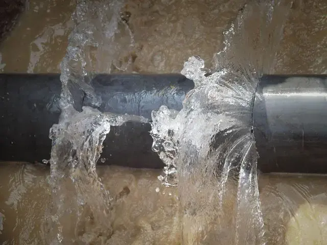 Water spraying from a split supply pipe over a flooded floor
