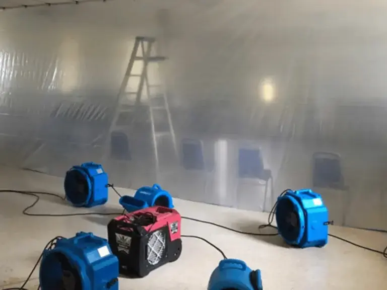 Air movers and a dehumidifier drying a commercial space behind plastic containment