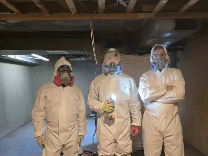 Three workers in protective suits and respirators in a basement during a sewage cleanup