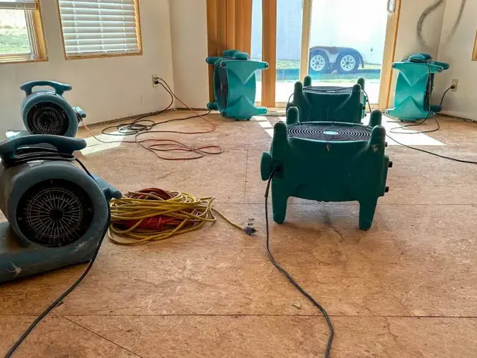 Air movers and a dehumidifier drying a room with the flooring pulled back